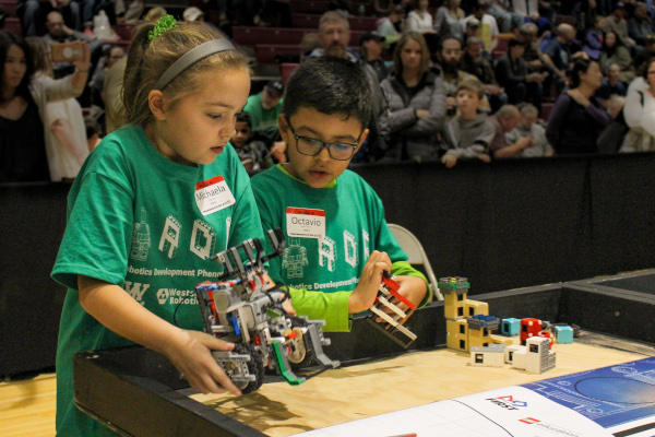 students placing a LEGO robot on the playing field