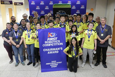 a group of students posing with medals, trophies, and a large blue banner celebrating winning an event
