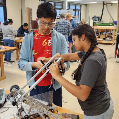 a student cutting a piece of plastic on a band saw while another student watches