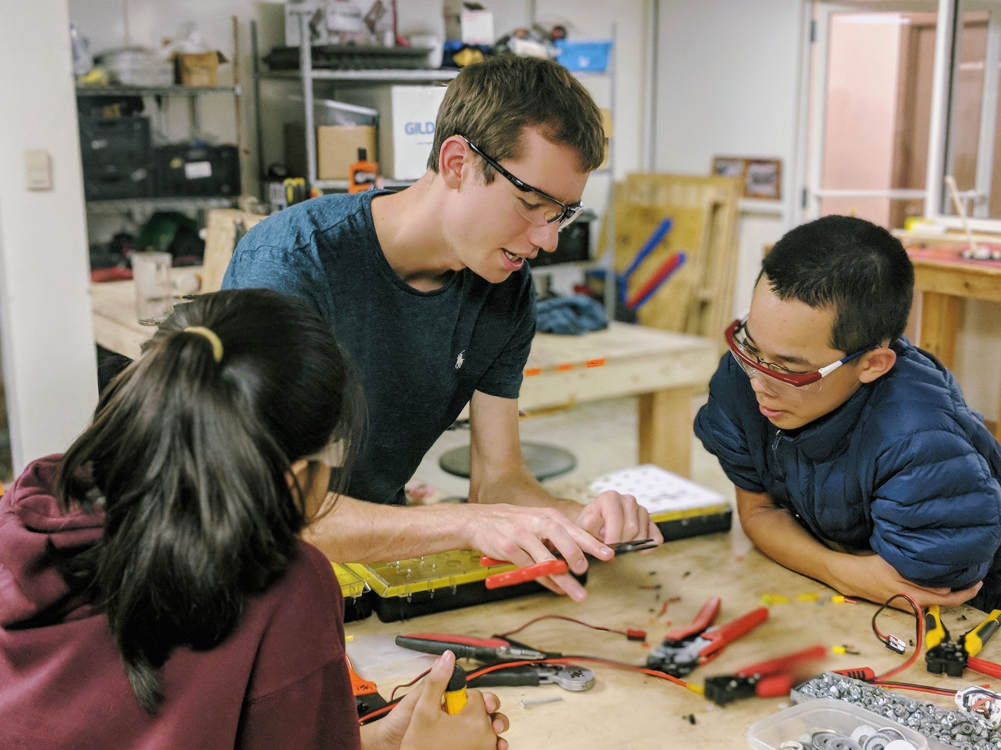a mentor showing a pair of students how to use a tool